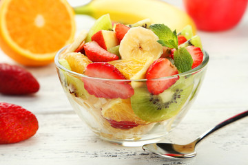 Fresh fruit salad in bowl on white wooden background