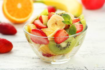 Fresh fruit salad in bowl on white wooden background