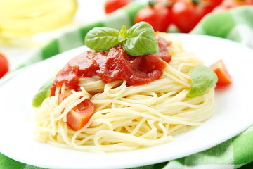Spaghetti with tomatoes and basil on plate on white wooden backg