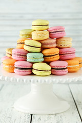 French colorful macarons on cake stand on white wooden backgroun