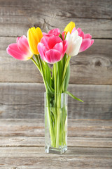 Beautiful tulips in vase on grey wooden background