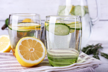 Fresh water with lemon and cucumber in glassware on wooden table, closeup
