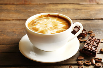 Cup of coffee latte art with grains and chocolate on wooden background