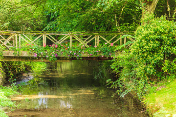 Fototapeta na wymiar Old small bridge over river in green garden.
