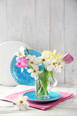 Spring bouquet in glass mug on color wooden background
