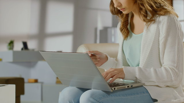 Young lady checking balance on bank account using laptop, card
