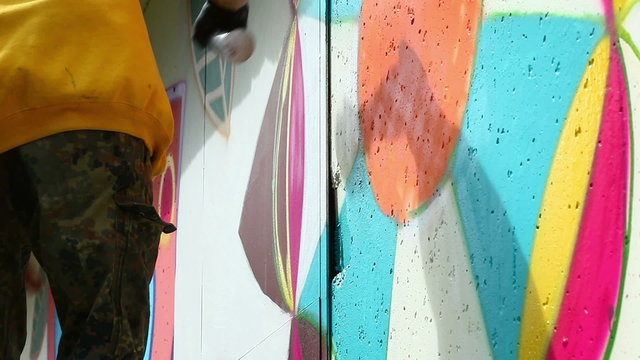 Young man drawing graffiti on wall with spray can