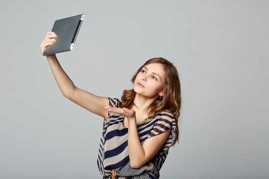 Young woman taking selfie with digital tablet, on gray backgroun