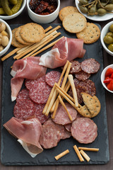 Assorted meat snacks and pickles on a blackboard, top view