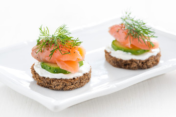 canape with cheese, cucumber and salted salmon on white plate