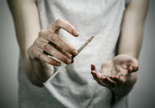 skinny dirty addict holding a syringe with a drug in studio