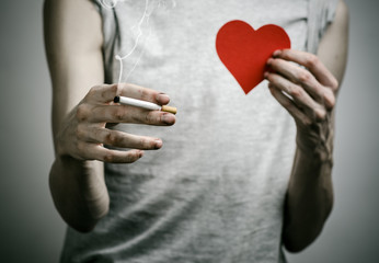 smoker holds the cigarette in his hand and a red heart in studio