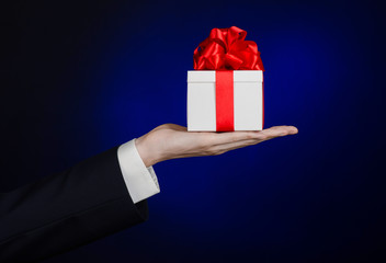 man in a black suit holding gift wrapped in white box in studio