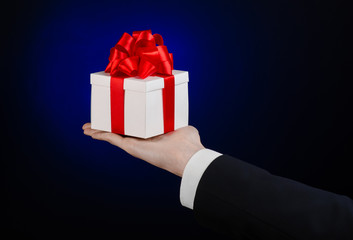 man in a black suit holding gift wrapped in white box in studio