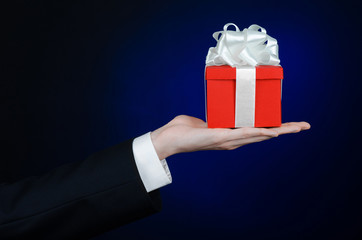 man in a black suit holding gift wrapped in red box