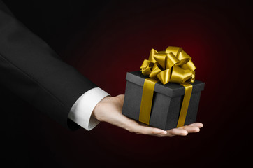 man in a black suit holding gift packaged in a black box with