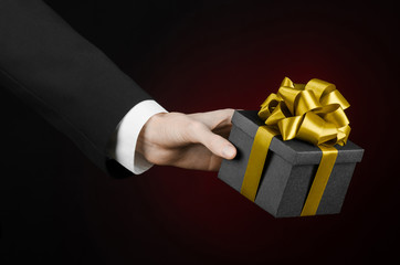man in a black suit holding gift packaged in a black box with