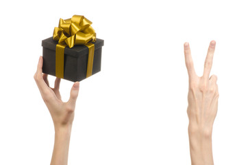 hand holding a gift wrapped in a black box with gold ribbon