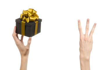 hand holding a gift wrapped in a black box with gold ribbon