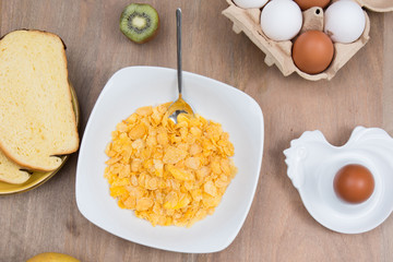 Cornflakes with milk, eggs,  on a wooden brown background