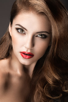 Beautiful woman with evening make-up, red lips and curls. Beauty face. Picture taken in the studio on a gray background.