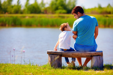 happy father and son sitting on the river bank