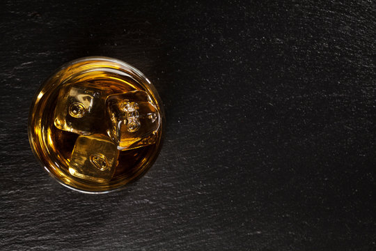 Glass of whiskey with ice on black stone