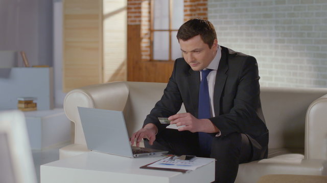 Rich man business suit inserting credit card number on laptop