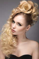 Fototapeta premium Piękna blondynki dziewczyna w wieczór sukni z niezwykłą fryzurą w postaci róż i jaskrawego makeup. Piękna twarz. Zdjęcie zrobione w studio na szarym tle.