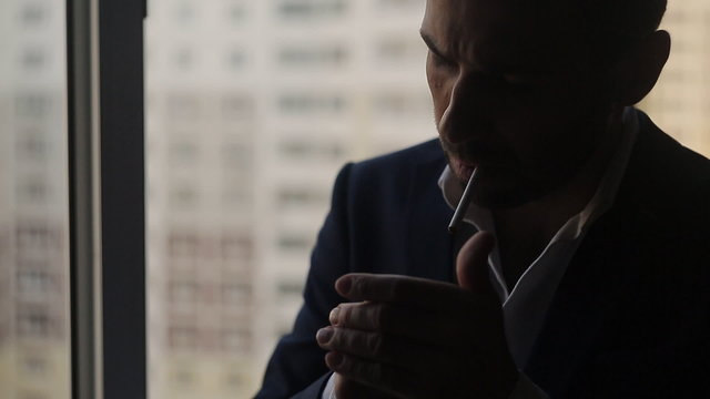 man in suit lights a cigarette at the window