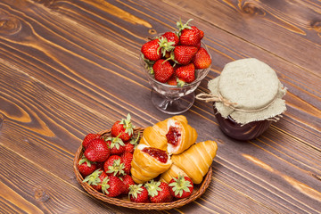 Strawberries and croissant on a wooden brown background