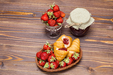 Strawberries and croissant on a wooden brown background