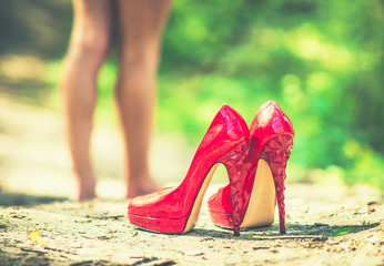 Red high heels with barefoot girl on background