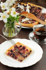 Square piece of berry pie served with tea in glass cup and white