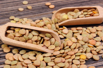Heap of green lentil with spoon on wooden background