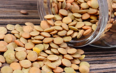 Lentil spilling out of glass jar. Wooden background