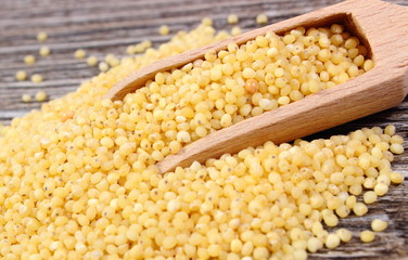 Heap of millet groats with spoon on wooden background