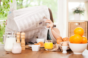 Woman is reading a newspaper while having breakfast