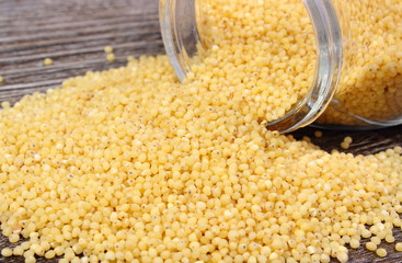 Millet groats spilling out of glass jar. Wooden background