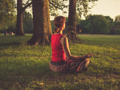 Woman meditating in park at sunset