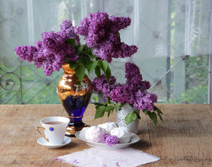 Fototapeta na wymiar Tea in a porcelain cup, a zephyr and a lilac bouquet in a beauti