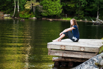 teenage girl sitting on a dock beside a lake