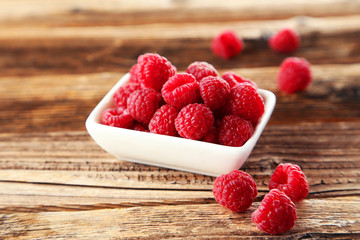 Raspberries in bowl on brown wooden background