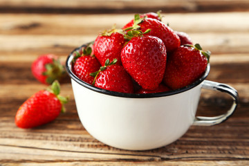 Strawberries in cup on brown wooden background