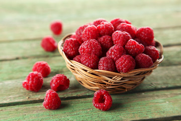 Raspberries in basket on green wooden background