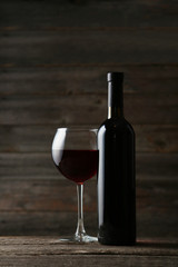 Red wine glass with bottle on grey wooden background