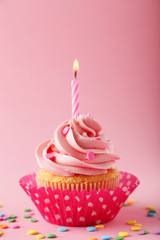 Tasty cupcake with candle on pink background