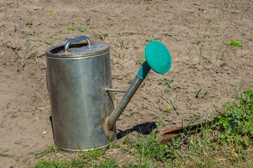 металлическая лейка с зелёной насадкой стоит на грядке