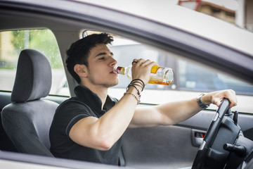 Young man driving his car while drinking alcohol