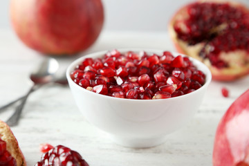 Delicious pomegranate fruit in bowl on white wooden background